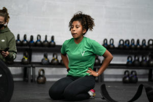 Female athlete takes a breather in the seated position on her knees, hands on hips.