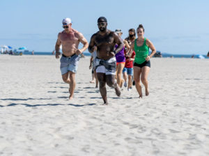 Athletes running on the sand at the beach.
