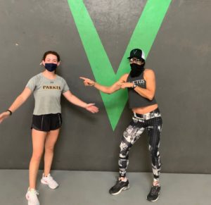 Two women posing in front of the Invictus V logo at the gym.