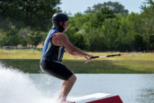 Male masters athlete barefoot waterskiing up a ski ramp.